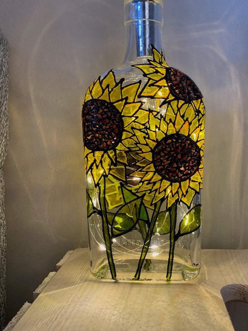 Large yellow sunflowers stand the full height of the bottle all the way around. Painted on a recycled bottle with acrylic paint. The bottle is lit with fairy lights from within.