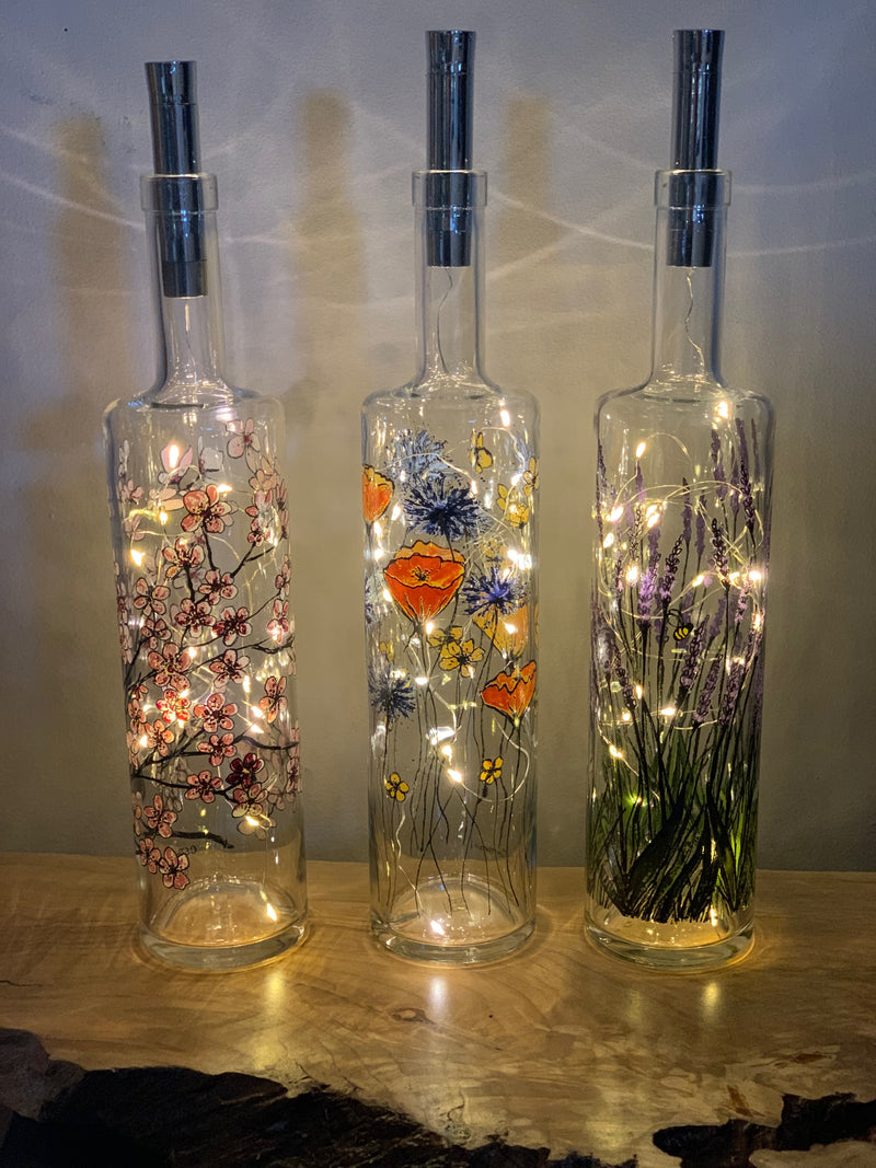 3 Printed Bottles with Fairy Lights. From left to right, they are 'Blossom Branch', 'Monet's Garden' and 'Lavender and Bees'