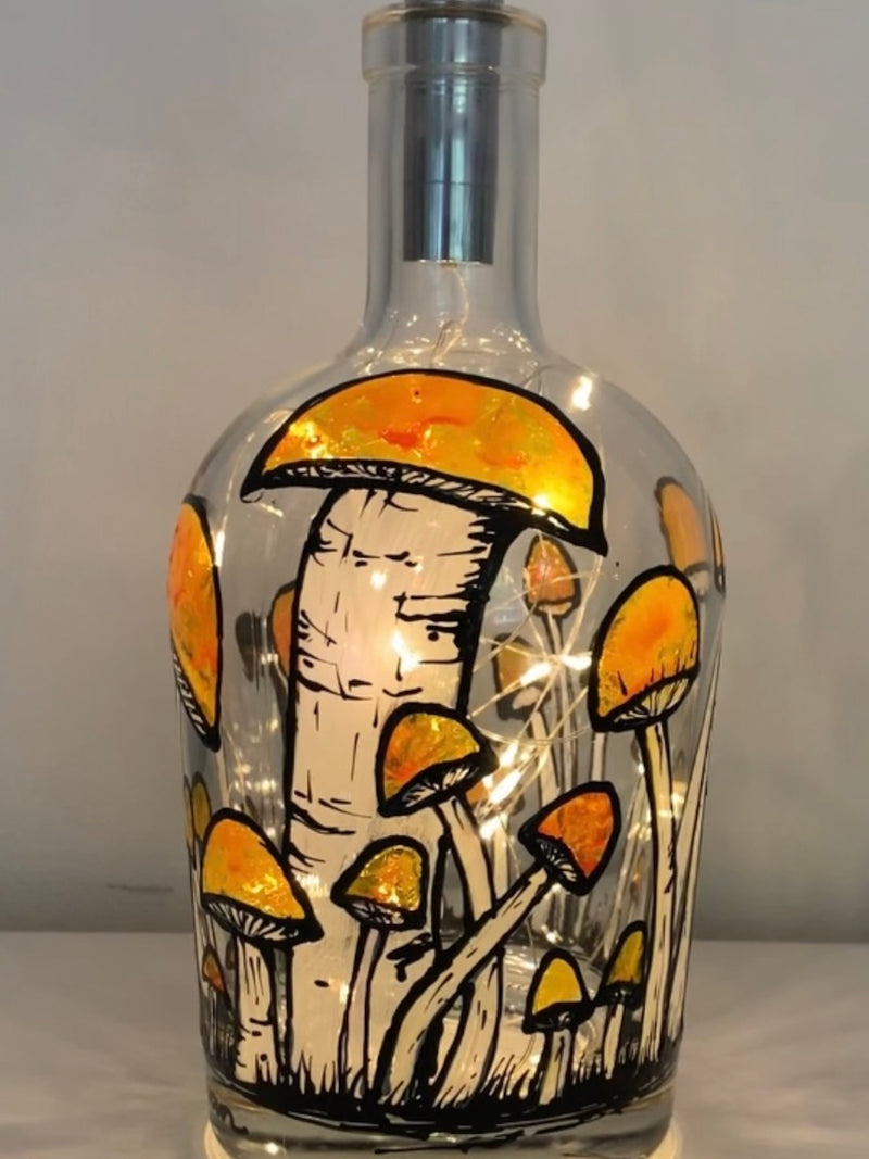 Numerous large and small mushrooms with clementine or red caps surround this bottle. Painted on a recycled bottle with acrylic paint. The bottle is lit with fairy lights from within.