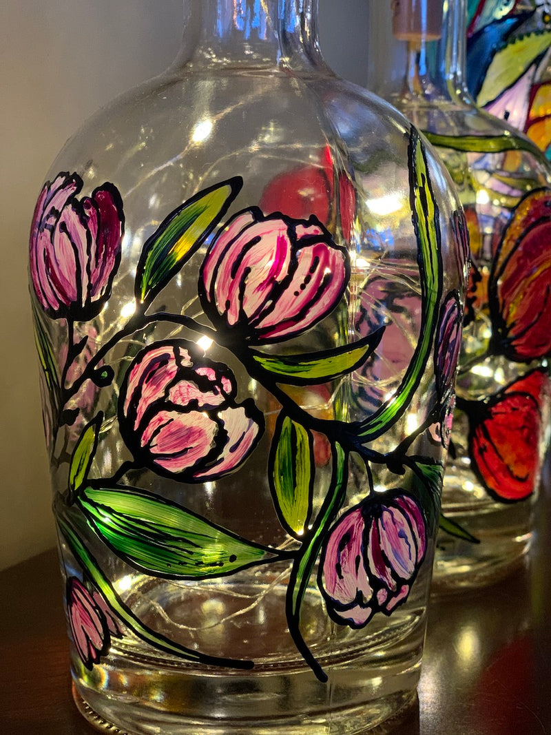 Flowers bloom off a vine that wraps around this bottle. Painted on a recycled bottle with acrylic paint. The bottle is lit with fairy lights from within.
