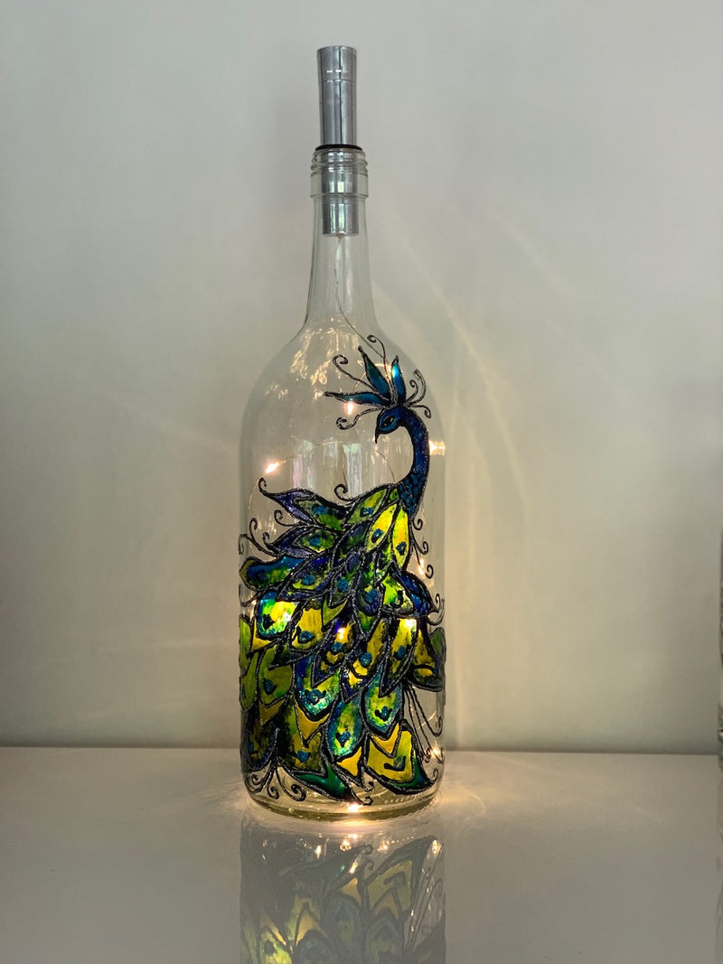 A slendid colourful peacock shows off his tail feathers. Painted on a recycled bottle with acrylic paint. The bottle is lit with fairy lights from within.