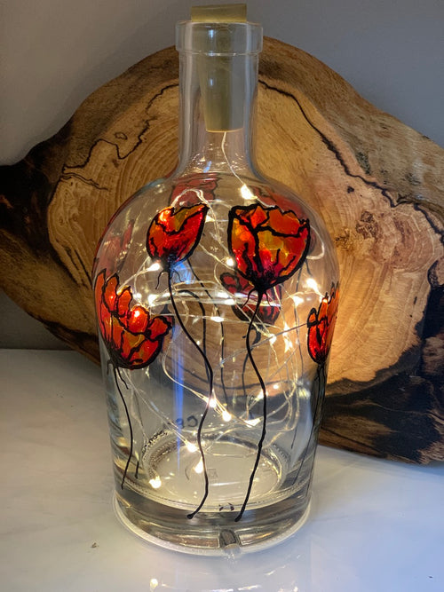 Red poppies with long stems reach from bottom to top of this whiskey bottle. Painted on a recycled bottle with acrylic paint. The bottle is lit with fairy lights from within.
