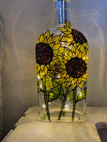 Large yellow sunflowers stand the full height of the bottle all the way around. Painted on a recycled bottle with acrylic paint. The bottle is lit with fairy lights from within.