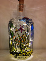 A colourful underwater scene has jellyfish, seahorses, fish and starfish swimming through the seaweed. Painted on a recycled bottle with acrylic paint. The bottle is lit with fairy lights from within.